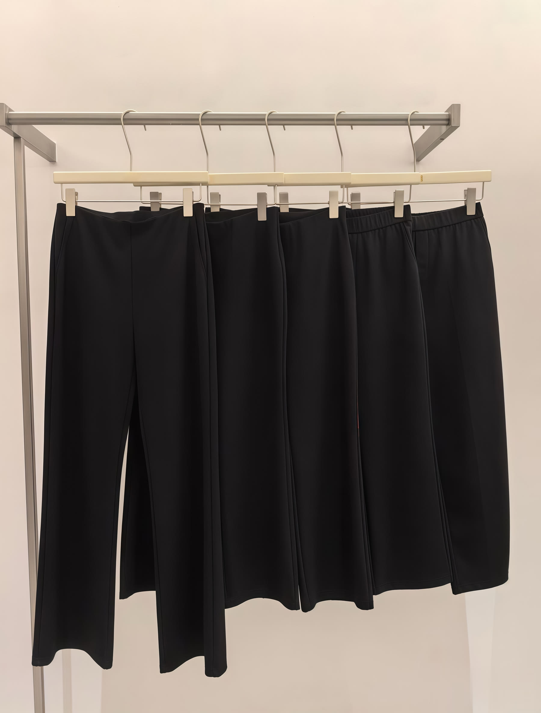 Four black trouser and skirt silhouettes displayed on a garment rack